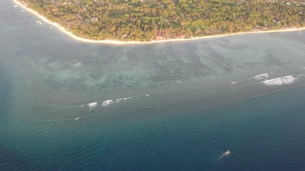 Approaching the island the camera looks down visible coral reef and palm trees on the shore gili air — Stock Video