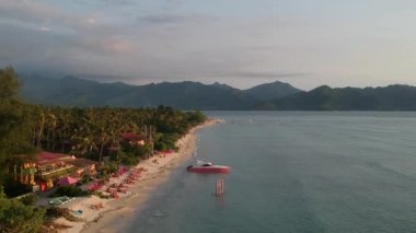 Gün batımında sahil boyunca uçmak ve resimli dağların arka planında pembe bir tekne