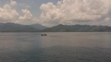 Lombok adasının dağlarının arka planına karşı okyanusta seyreden büyük bir tekne.
