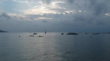 Bulutlu bir havada gün batımında teknelerle tekneler arasında süzülüyor.