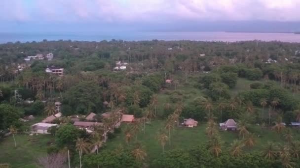 El dron aterriza durante una puesta de sol de color rosa azulado, una isla con palmeras y algunas casas es visible — Vídeos de Stock