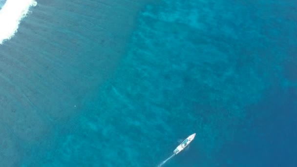 Ram från drönaren vertikalt ner på det turkosblå havet längs vilken en vit båt flyter — Stockvideo