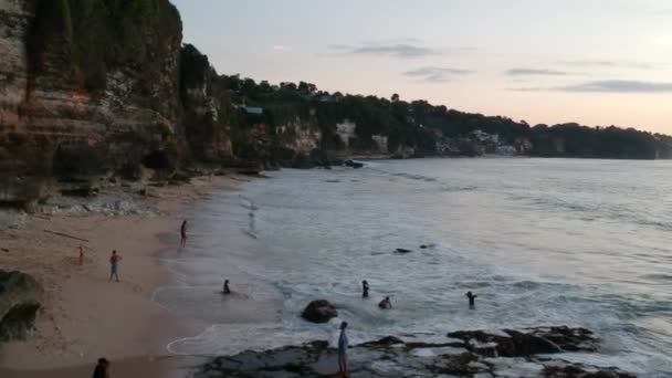 Drönare flyger längs en klippa med en strand där människor går Dreamland beach bali indonesia — Stockvideo