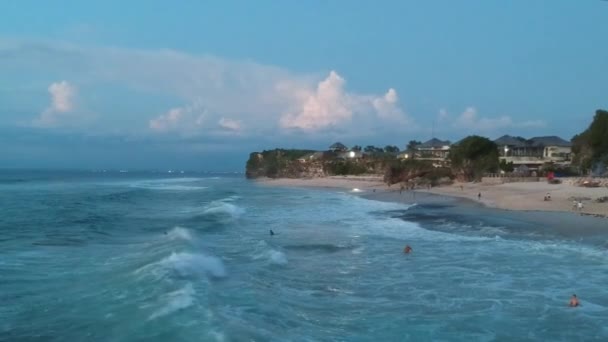 Vol de drone le long de la côte de l'océan avec des vagues moussantes au coucher du soleil dans la soirée contre un ciel bleu et une falaise — Video