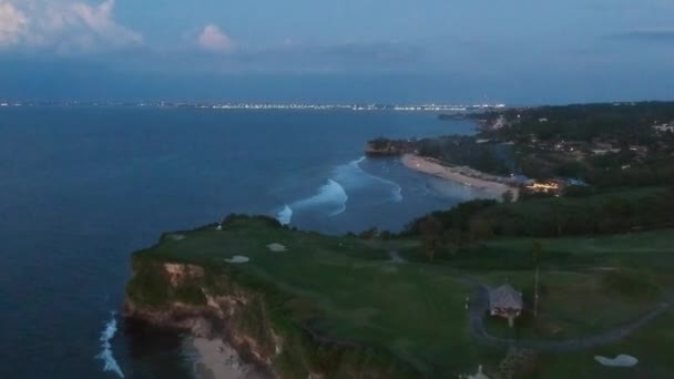 Despegar en un avión no tripulado más allá de un acantilado con vistas a una playa de arena por la noche con luces en el horizonte — Vídeos de Stock