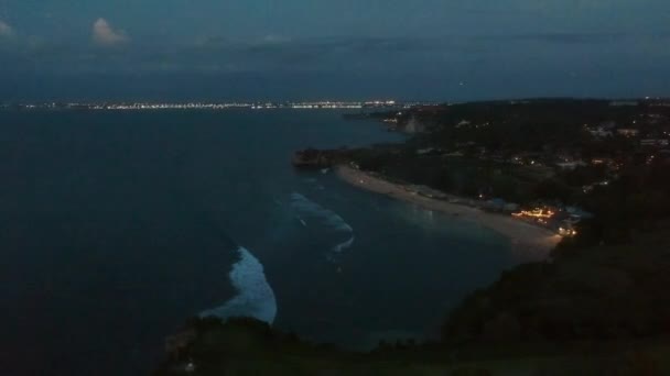 Falaise surplombant une plage de sable la nuit avec des lumières à l'horizon — Video