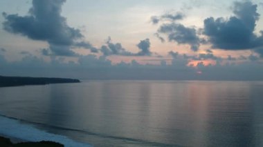 İnsansız hava aracı okyanusun arka planına dikey olarak havalanıyor ve pembe güneşli bulutlu günbatımına doğru.