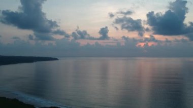 İnsansız hava aracı okyanusun arka planına doğru uçar ve pembe güneşli bulutlu günbatımına doğru.