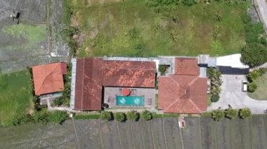 Güneşli havalarda pirinç tarlalarının ortasında kırmızı çatılı bir evin üzerinde dikey uçan bir kameranın sürati.