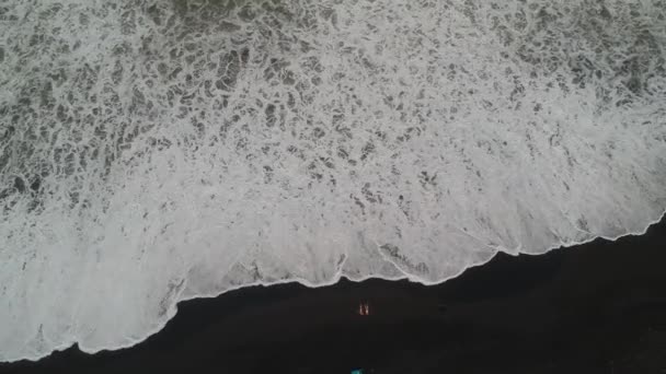 Камера літає вертикально з пляжу з чорним піском і величезними білими океанськими хвилями — стокове відео