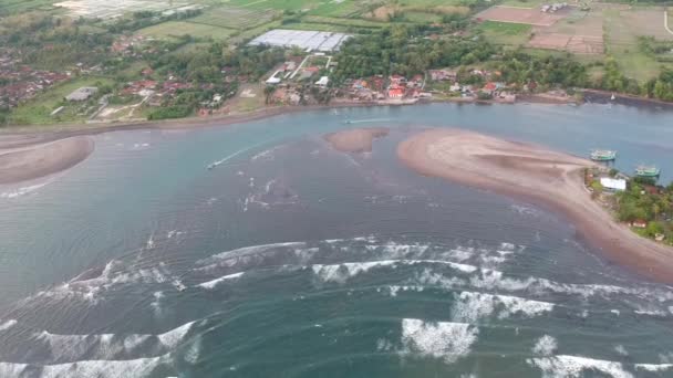 La cámara vuela desde un hermoso lecho de río que fluye hacia el océano con grandes olas y barcos de pesca navegan Península Prancak Perancak Bali — Vídeos de Stock