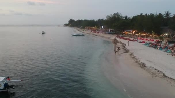 Zoom telecamere lungo la riva sabbiosa con caffè e luci serali e persone in aria swing gili — Video Stock