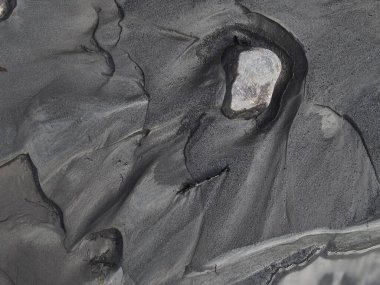 Nehirdeki bir taşın etrafında siyah kum desenleri       