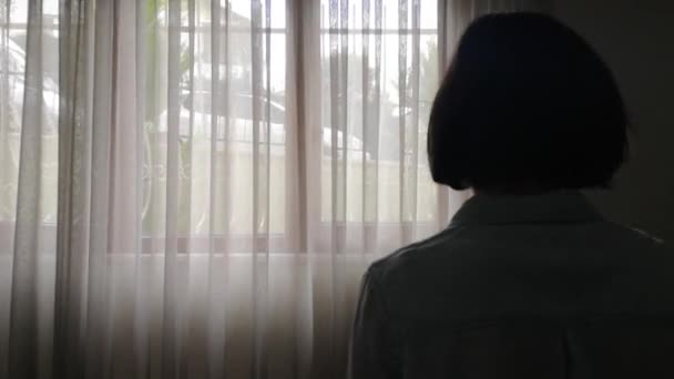Молодая женщина в медицинской маске смотрит в окно — стоковое видео