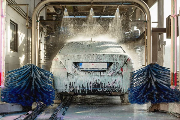 Trabajador de lavado de coches con espuma activa en un túnel de lavado.