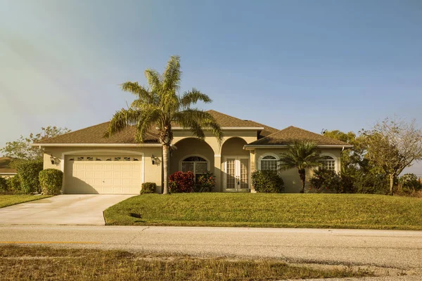 South Florida single family house in sunny day. Typical Southwest Florida concrete block and stucco home in the countryside with palm trees, tropical plants and flowers, grass lawn and pine trees. Flo