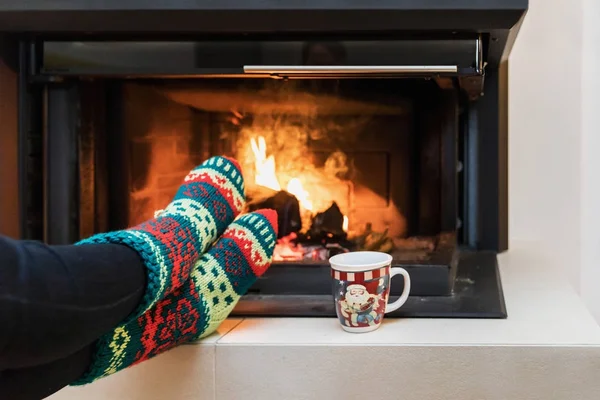 Feet in woollen socks and mug by the Christmas fireplace. Close