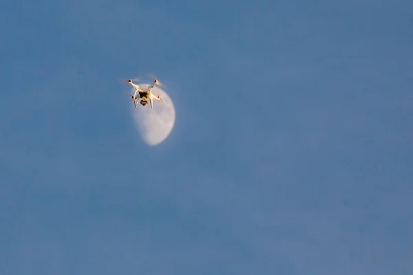 Flying white dron on sky in background moon. Dron looks like he\'s landing on the moon.