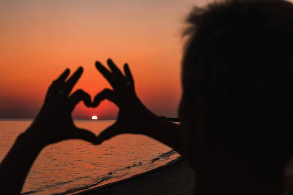 Primer plano del corazón hecho por las manos femeninas fondo del mar puesta del sol — Foto de Stock