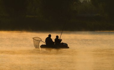 Sabah erkenden. Teknedeki balıkçılar. Nehrin üstünde buhar var. Güneşin doğuşu nehri sıcacık tonlarda aydınlattı..