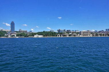 İstanbul Boğazı 'ndan İstanbul Panoraması. Martılar mavi suyun üzerinde uçar. Modern yüksek binalar ve eski tarihi bir saray görülebilir. Mavi gökyüzündeki bulutlar.