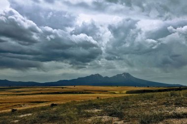     Fırtına bulutları volkanın üzerinde toplanıyor. Güzel Hasan volkanı buğday tarlalarının yanındaki ovada yükselir. Dağın tepesinde kasvetli bulutlar asılı. Korkutucu.                           
