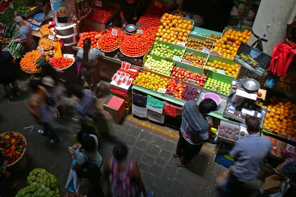 Busy island farmers market with fresh fruits and vegetables. Shop owners chatting with tourists and locals.