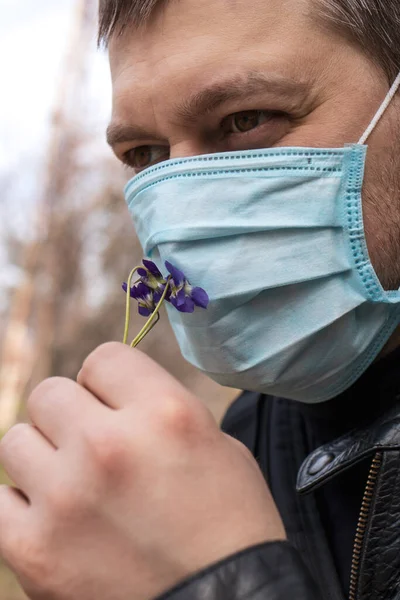 Man in medical mask sniffing flowers in the forest.