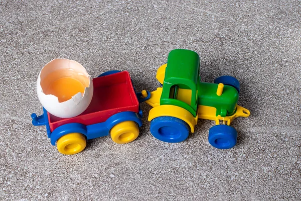 A toy tractor carries two chicken eggs. Plastic and natural food.