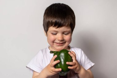 Küçük bir çocuk elinde yeşil bir biber tutuyor ve gülümsüyor. Düzgün beslenme ve çocuklar için sağlıklı yaşam tarzı. Çocukların diyetinde sebzeler.