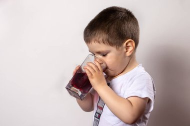 Küçük bir çocuk bardaktan kiraz suyu içiyor. Çocukların beslenme düzeninde meyve suyu ve vitaminler.