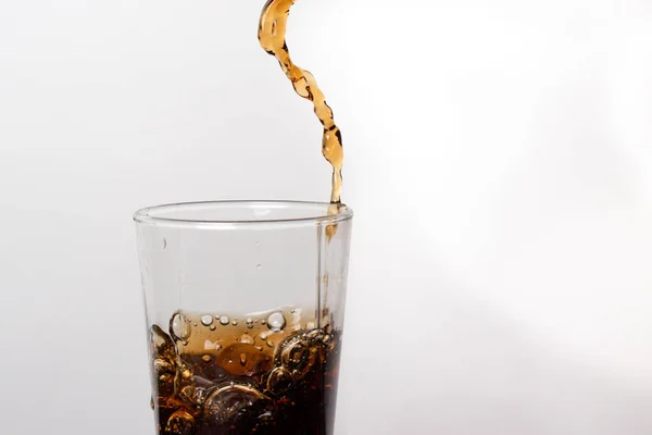 Brown carbonated drink is poured into a glass. Bubbles of sweet liquid. Sugar in drinks.