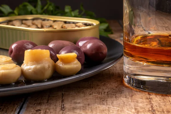 Whiskey in a glass and an appetizer for alcohol: pickled champignons, olives, sprats. Snack for whiskey, cognac, brandy. — Stock Image Whiskey Glass Appetizer Alcohol Pickled Champignons Olives Sprats Snack Whiskey Stock Photo