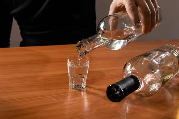 A man pours vodka from a bottle into a glass. Alcoholism.
