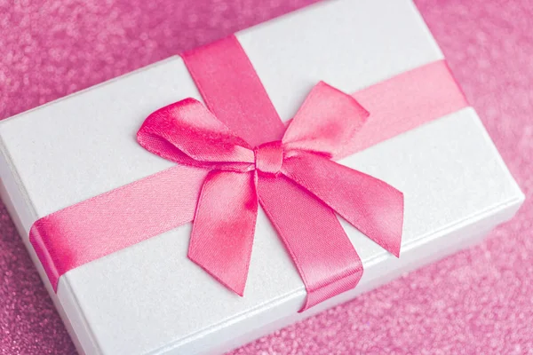 Present paper box with pink bow on glitter background
