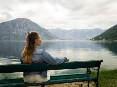Bankta oturan bir kız Kotor Bay manzarasına hayran. Karadağ 2019 sonbaharında