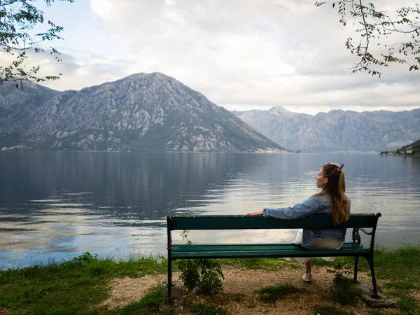 Bankta oturan bir kız Kotor Bay manzarasına hayran. Karadağ 2019 sonbaharında