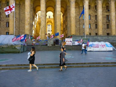 Yoldan geçenler Gürcistan parlamentosunun önünden geçiyor. Gürcistan, ABD ve AET Hang bayrakları. Mayıs güneşli bir gün. Tiflis, Georgia Caddesi..
