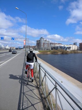 Bisikletçi otobanın yanındaki tırabzanda dinleniyor. Rusya 'da güneşli bir gün. Finlandiya Körfezi sağ tarafta görülebilir..