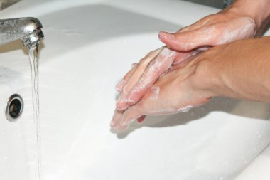 Eller, beyaz bir lavabonun üzerinde sabunla yıkanır.