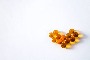 Sarı vitamin kapsülleri Omega 3 yağ asitleri, kalp şeklinde bağışıklık ve hastalık önleme için izole edilmiş beyaz bir zemin üzerinde bir masanın üzerinde yatar.
