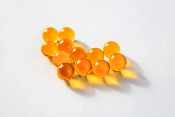 Sarı vitamin kapsülleri Omega 3 yağ asitleri, kalp şeklinde bağışıklık ve hastalık önleme için izole edilmiş beyaz bir zemin üzerinde bir masanın üzerinde yatar.