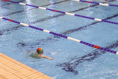 Çocuklar havuzda yüzmeyi öğrenirler. Havuzda yüzme dersi sırasında gözlerinde yüzmek için gözlük olan küçük çocuk.