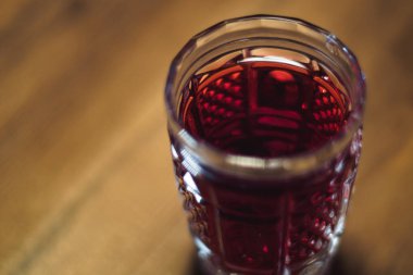 Kristal bir bardaktaki kırmızı tentür ahşap bir masada duruyor.