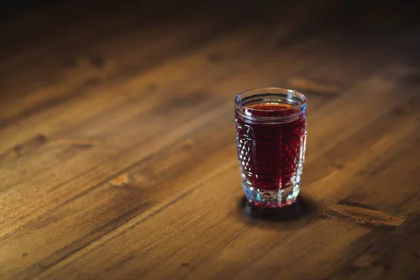 ガラスの中の赤い色の色合いは 木製のテーブルの上に立つ — ストック写真