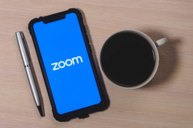 Ekran akıllı telefonundaki uygulama logosunu yakınlaştır. Zoom Video Communications, uzaktan konferans hizmeti veren bir şirket. Bir fincan kahve ve kalem..