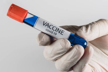 Elinde mavi renkli Covid-19 aşısı olan bir vakum tüpü ve beyaz arka planda tıbbi bir eldiven.