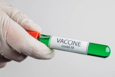 Elinde yeşil renkli Covid-19 aşısı olan bir vakum tüpü ve beyaz bir arka planda tıbbi eldiven.