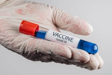 Elinde mavi renkli Covid-19 aşısı olan bir vakum tüpü ve beyaz arka planda tıbbi bir eldiven.