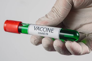 Elinde yeşil renkli Covid-19 aşısı olan bir vakum tüpü ve beyaz bir arka planda tıbbi eldiven.